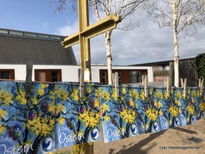 Ein Kreuz im Freien - dahinter Birken - an einer Wäscheleine hängen Karten mit Frohe Ostern