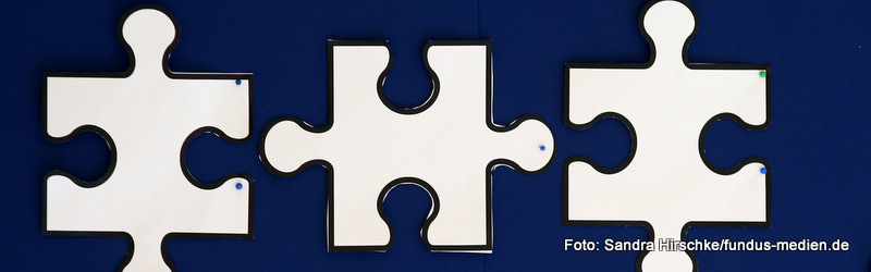 Weiße Puzzleteile auf dunkellila Untergrund. Liegen in zwei Spalten mit links drei und rechts zwei Stück. Sie sind nicht zusammengesteckt, würden aber so, wie sie liegen, ineinander passen.