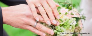 Hände eines Brautpaars - die Hände liegen auf dem Brautstrauß.