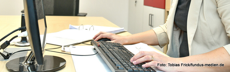 Hände einer Frau liegen auf einer PC-Tastatur - der Anschnitt eines PC-Monitors - Bürosituation