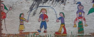 Graffiti an einer weißen Backsteinwand - Zeichnungen von spielenden Kindern, beim Bockspringen und Seilhüpfen